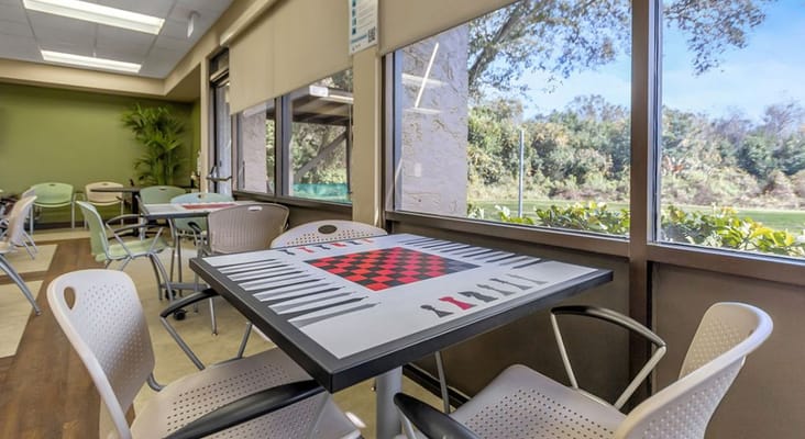 Table with checkerboard design in a common area surrounded by chairs and large windows