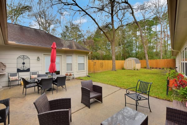 Backyard seating area with tables and chairs under a red umbrella.