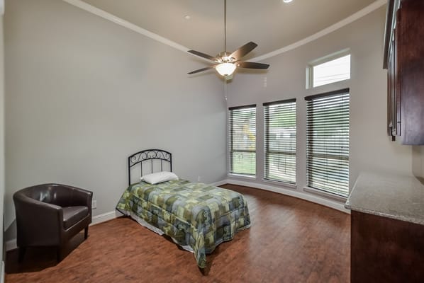A cozy bedroom with a bed, chair, and large windows.