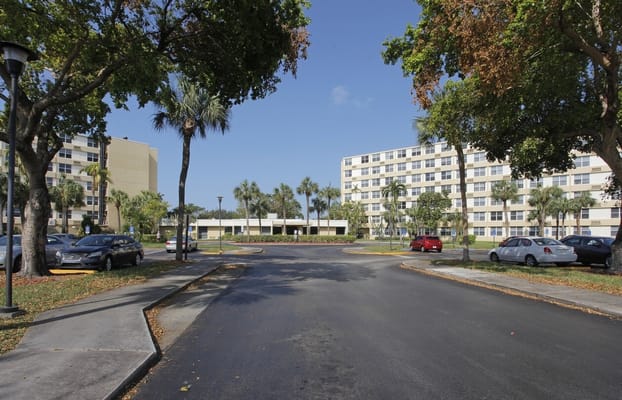 View of the main entrance area at St. Andrews Towers with palm trees and parking lot.
