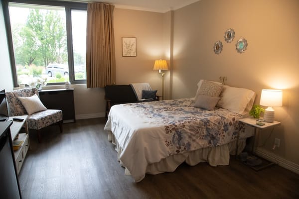 A well-decorated bedroom featuring a bed, seating area, and natural light from large windows.
