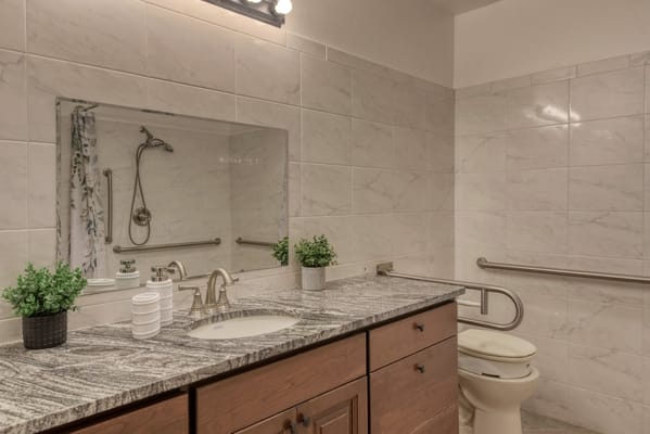 A well-lit bathroom featuring a sink, toilet, and grab bars for safety.