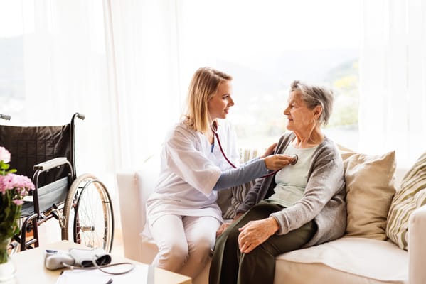 Nurse examining a senior resident in a bright living room