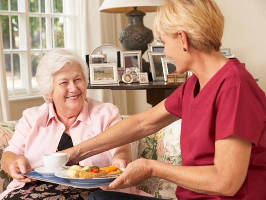 Caregiver serving food to a resident in a cozy living area