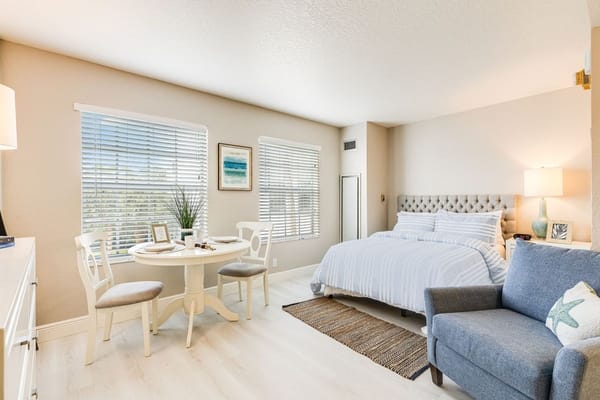 A bright and inviting studio apartment with a bed, dining table, and lounge area.