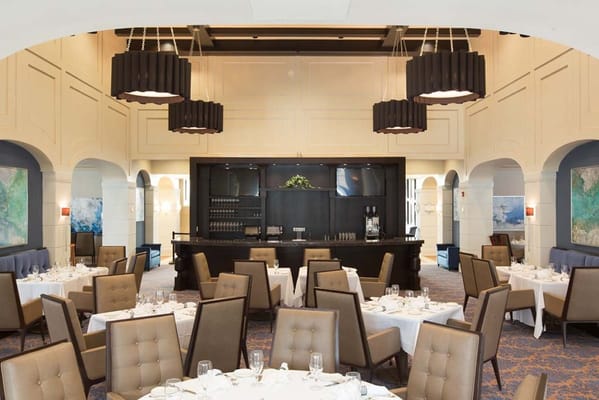 A spacious dining room with tables set for a meal, featuring modern chandeliers.