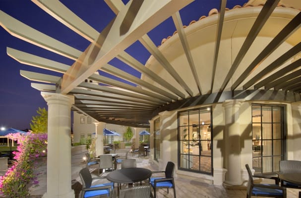 Outdoor patio area with tables and chairs under a modern pergola at night.