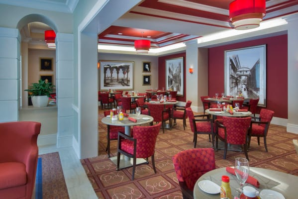 Elegant dining room with red decor and tables set for dining.