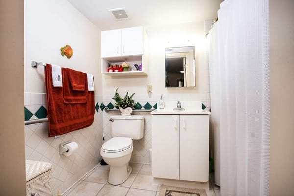 A clean bathroom featuring a white vanity, toilet, and orange towels.