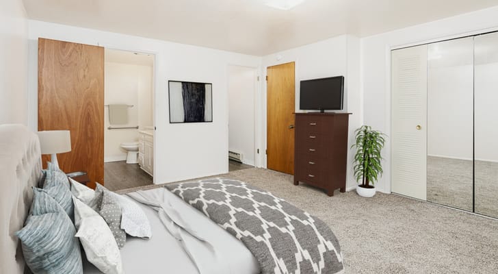 A cozy bedroom with a bed, dresser, and a bathroom door in the background.
