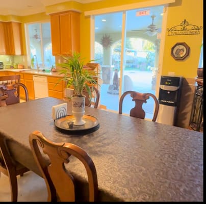 A dining table with chairs in a kitchen area, featuring a potted plant and sliding glass door.