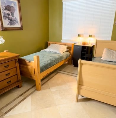 A cozy bedroom with two wooden beds, a dresser, and a window with blinds.