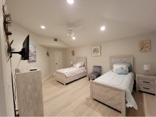 A spacious bedroom with two beds, a TV mounted on the wall, and modern decor.