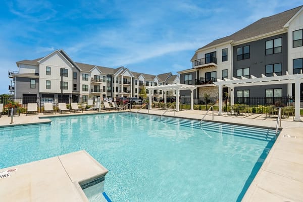 Sunny pool area with lounge chairs and apartment building in the background