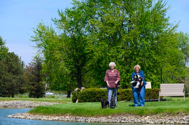 Two women walking dogs by a pond in a garden