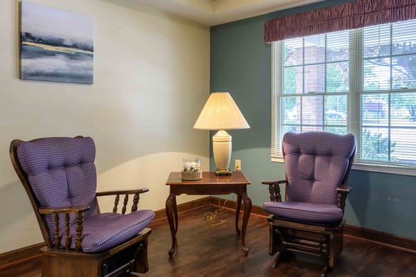 Two purple upholstered rocking chairs beside a table and lamp