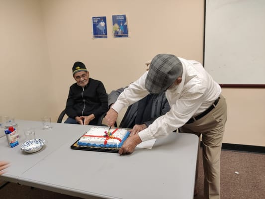 Resident cutting a birthday cake with another resident watching.