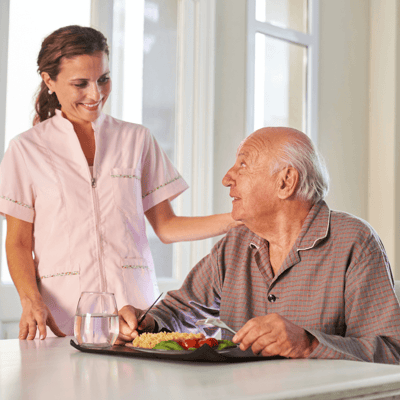 Caregiver interacting with an elderly resident at a dining table.