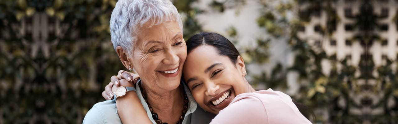 A senior woman smiles with a younger woman embracing her