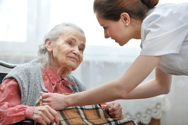 A caregiver assisting an elderly resident in a comfortable interior.