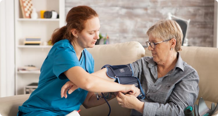A caregiver taking a resident's blood pressure in a cozy living room