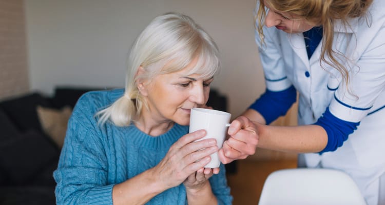 A caregiver assisting a resident with a cup of tea