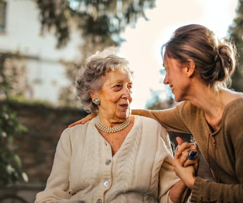 Elderly woman and caregiver sharing a joyful moment outdoors