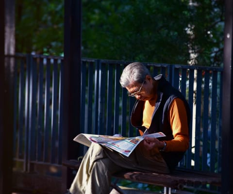 An elderly man reading a newspaper in a garden
