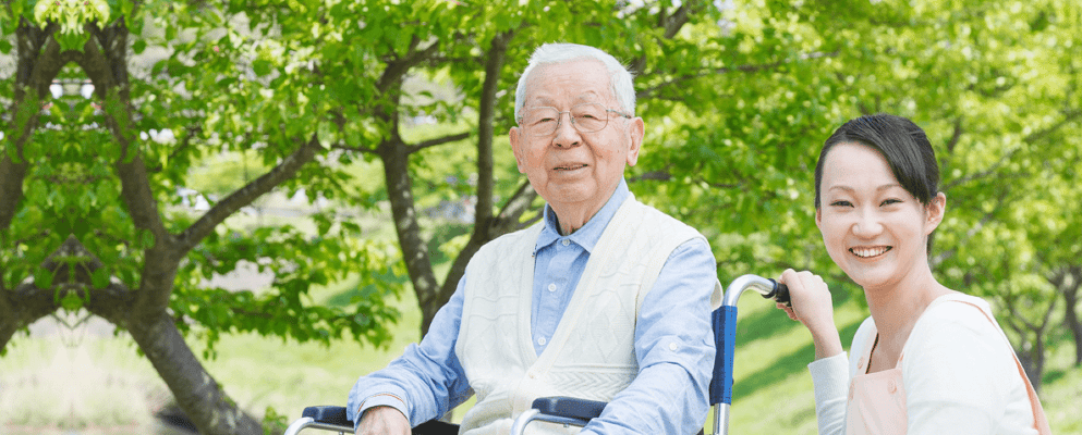 An elderly man smiling with a caregiver in a garden