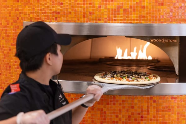 Staff member placing pizza in a wood-fired oven