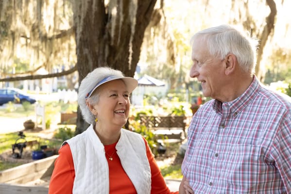 Two senior residents smiling outdoors under a tree