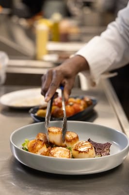 A chef preparing a plate of scallops in the kitchen