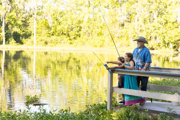 An elderly man fishing with a young girl by the lake