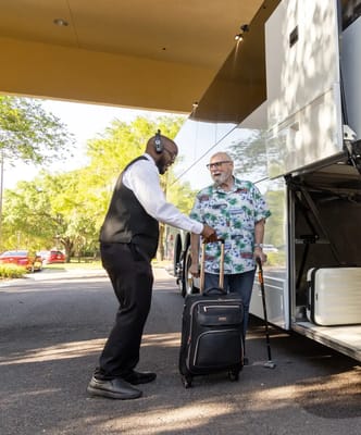 Staff assisting a resident with luggage near a transport vehicle