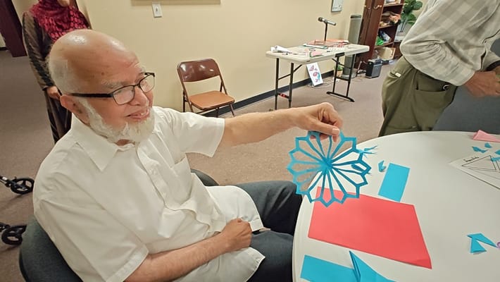 Senior resident holding a blue paper design at a table