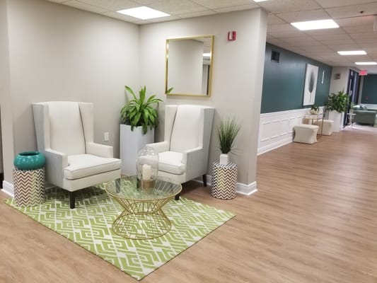 Lounge area with white chairs, green plants, and a glass table.