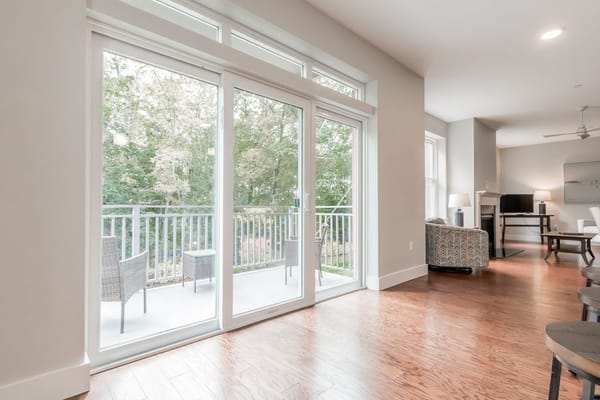 Living room featuring large glass doors opening to a balcony with a wooded view.