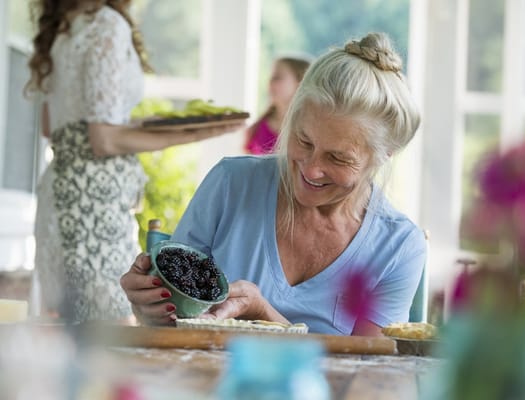 A senior woman joyfully baking with others in a sunny room