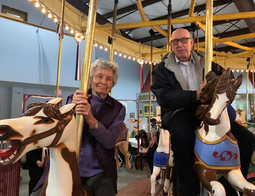 Two residents enjoying a carousel ride indoors