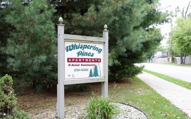 Sign for Whispering Pines Apartments in a garden setting