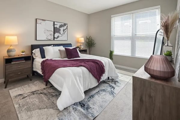 Cozy bedroom featuring a bed with a purple throw, bedside tables, and natural light