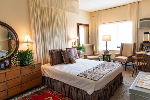 A well-decorated bedroom with a bed, chairs, and decorative plants.
