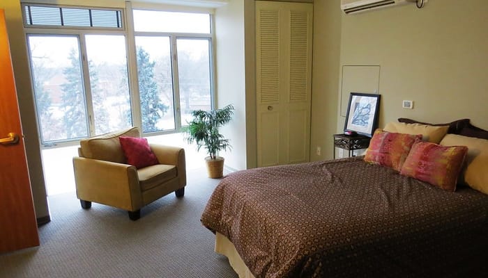 A spacious bedroom with a bed, chair, and large windows.