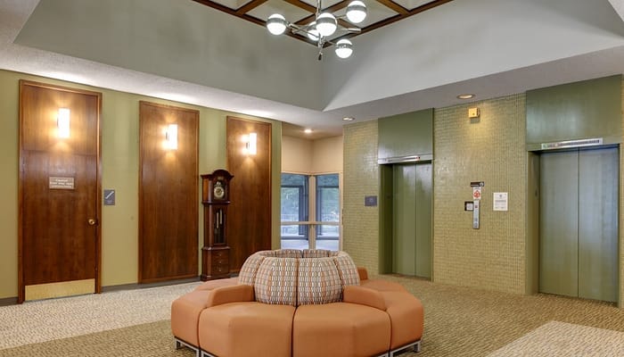 Cozy seating area in the lobby of Plymouth Place with elevators and wooden doors.