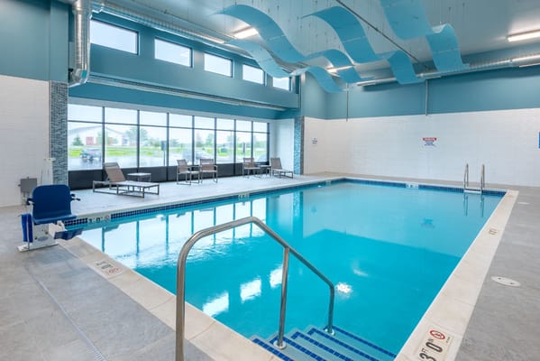Indoor swimming pool with seating and large windows.