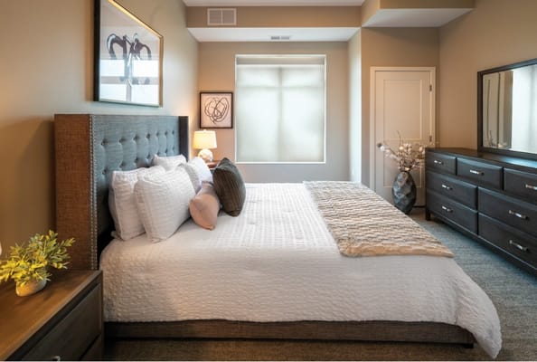 Well-decorated bedroom with a bed, dresser, and window light.