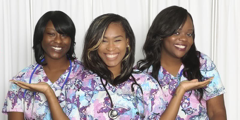 Three smiling caregivers in colorful scrubs