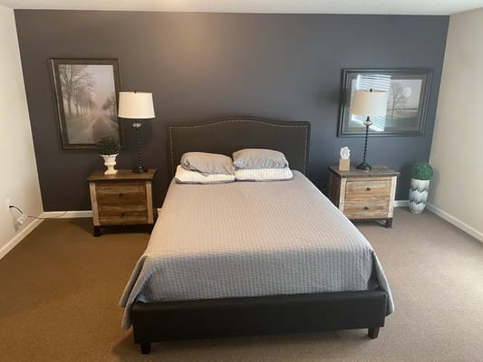 A comfortable bedroom with a bed, nightstands, and artwork on the walls.