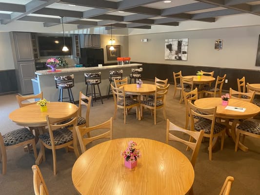Bright common area featuring round wooden tables with flowers.