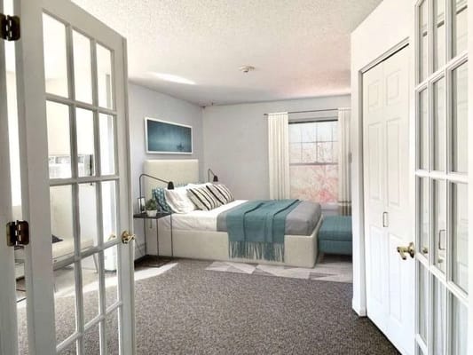 Spacious bedroom featuring a bed, sitting area, and natural light.